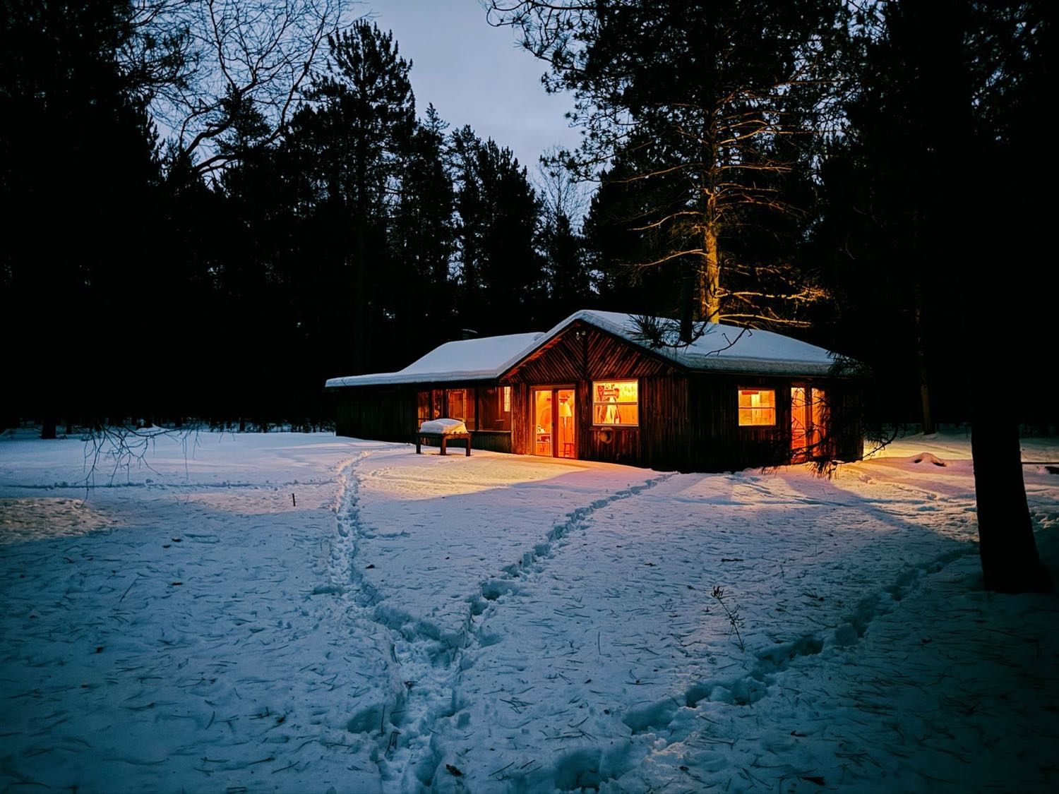 A low building with warmly lit windows standing in snow at dusk